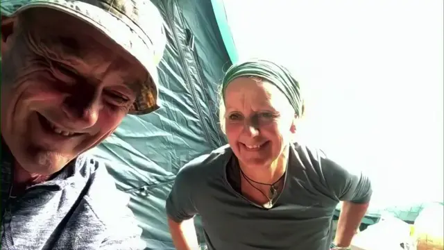 A man and woman in fleeces smile at the camera, they are sat inside a green coloured tent