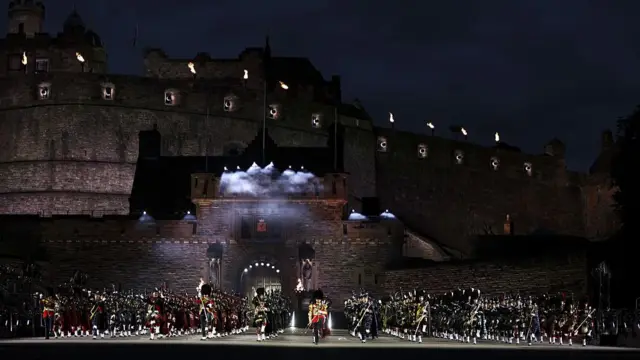 Wide shot of a Scottish military band in full tartan uniform performs with Edinburgh Castle in the background