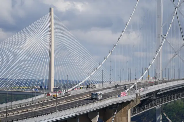 The Forth Road Bridge on a sunny day with a single-decker bus travelling across it.