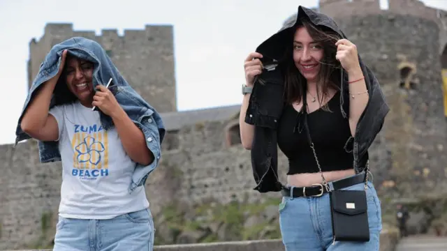 Two girls walking in rain, castle behind them, holding jackets over their heads.