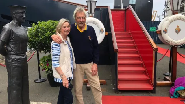 Susie Weston and David Hopikins stand before the Royal Yacht Britannia