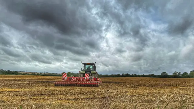 A tractor works on a field, grey cloudy sky above.