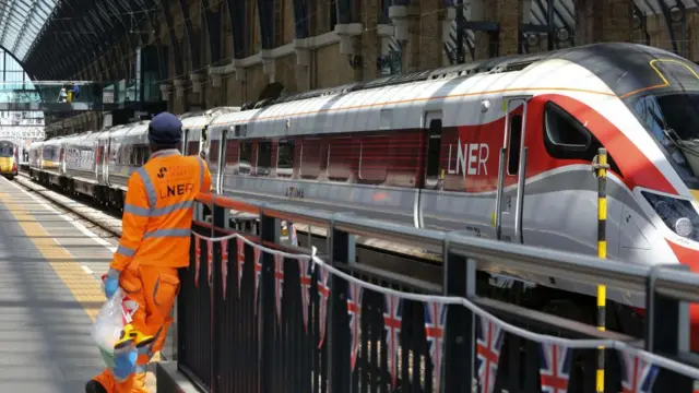 LNER train on platform, worker in orange outfit stands on the side of the tracks.