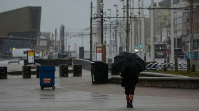 Person holding umbrella walking on rain swept Blackpool promenade