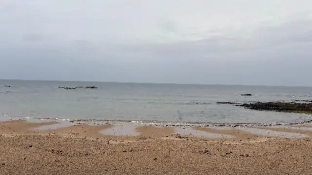 A beach in Scotland with grey sky and gloomy weather over the sea, rocks in the foreground.