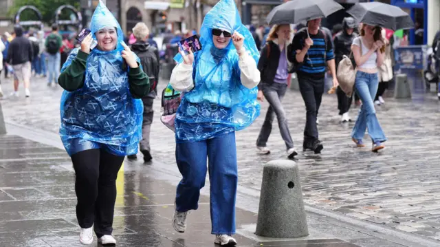 Two women wear blue ponchos amid strong rain and winds in Edinburgh