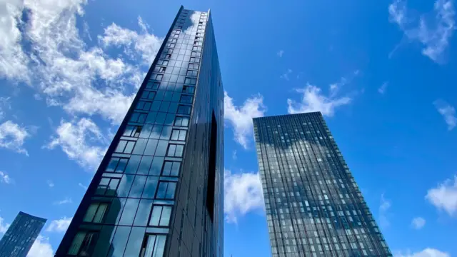 Large high-rise glass buildings in Manchester, blue skies above with only a few white clouds.