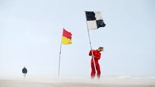 A lifeguard battles against the strong winds on Portsteward Strand in Northern Ireland, as she plants a warning flag advising swimmers against entering the water