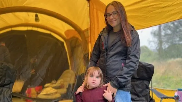 Daughter Isobel and mum Rebecca hold hands while posing against he backdrop of their yellow tent