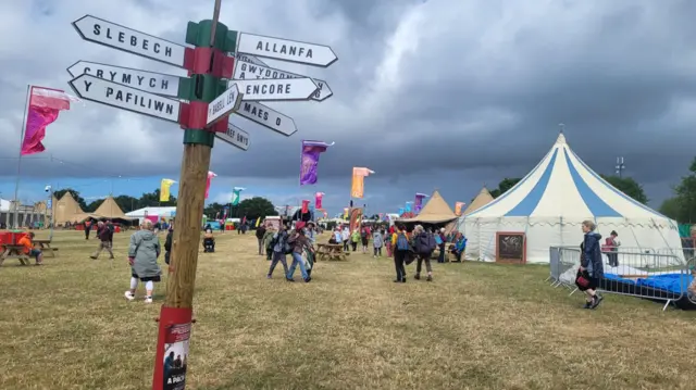 Picture of the Eisteddfod showing flags being blown and a leaning signpost
