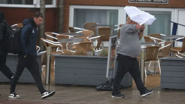 A man walks with an umbrella that is being blown towards him.