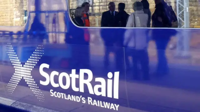 ScotRail train with company logo, window reflecting passengers on a platform