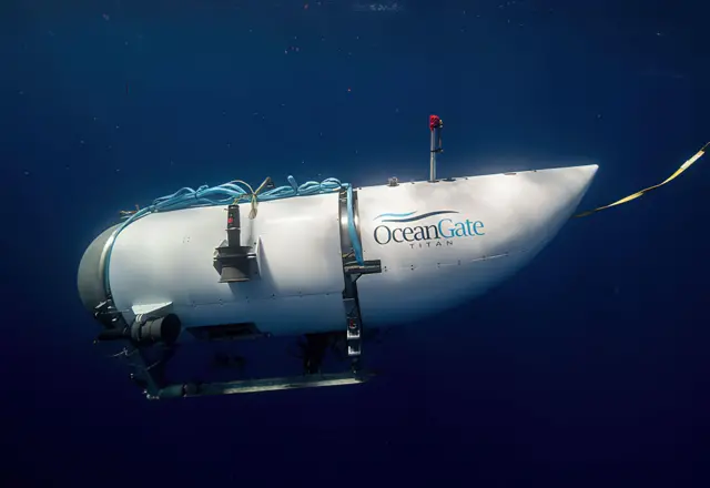 OceanGate submersible in the deep blue ocean. It's coloured white with a number of blue cables tied on top. A white cable leads behind it.