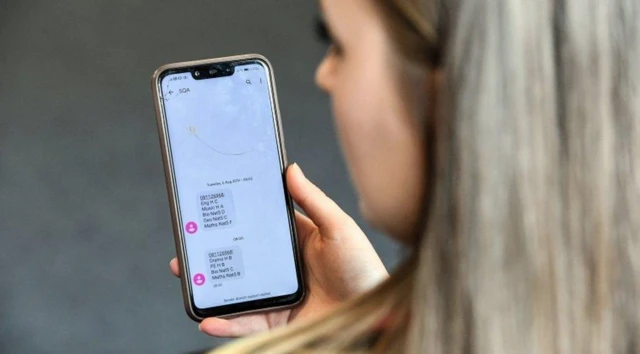 A teenage girl with long blond hair looks at exam results on a phone text message