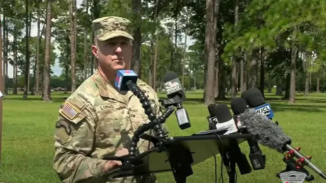 An man in Army uniform speaks to press from behind some microphones.