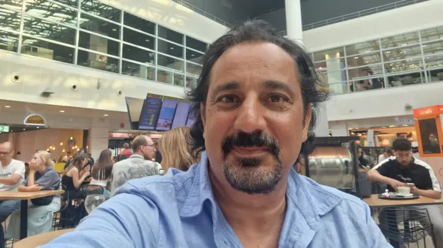 Man with a goatee beard takes a selfie in an airport lounge