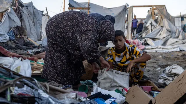 Two women and a boy look through debris in a Gaza camp