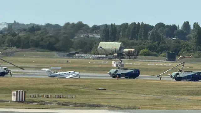 The plane on the tarmac, its tail sitting flat on the ground, surrounded by fire engines