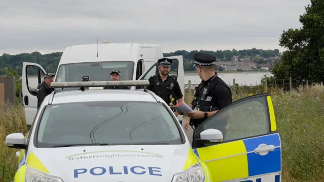 Five police officers stand around police vehicles in Brantham. The doors to the vehicles are open
