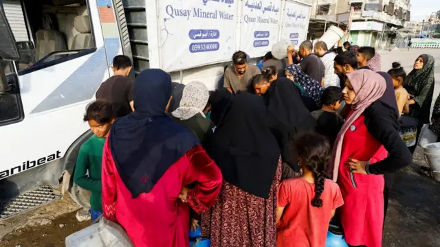 Palestinians stand with containers to collect water in Gaza City