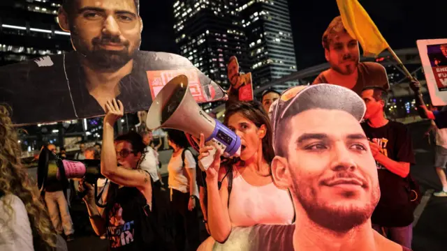 Woman shouts into megaphone during protest late at night. She's among a crowd holding large signs of people's faces