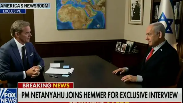 A screengrab of a Fox News interview with PM Netanyahu, who wears a suit and sits behind a desk, opposite a reporter.