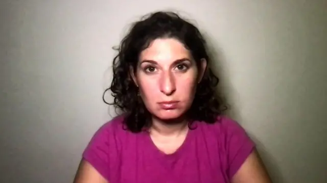A woman in a pink top looks at the camera