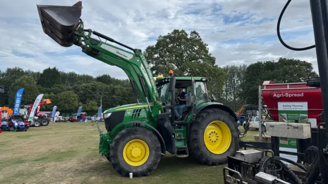 A large green and yellow John Deere tractor with its scoop held aloft