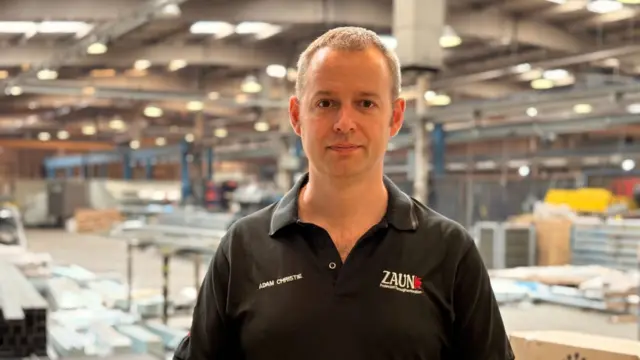 Man wearing black Zaun-branded polo shirt standing in the middle of a warehouse