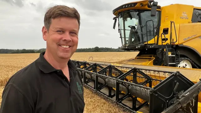 A man smiles in front of a yellow combine.