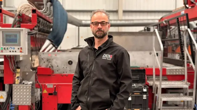 Man wearing black fleece branded for his company, Zaun, and standing in a workshop