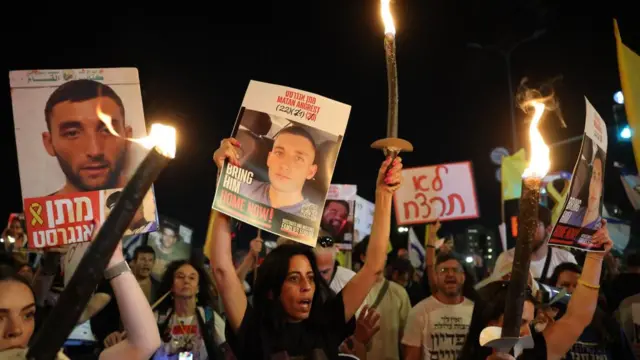 A crowd of people holding posters of hostages as well as tall torches on fire. It looks like they are chanting in unison