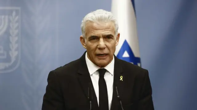 Headshot of Lapid speaking into two small microphones on stands in front of him.