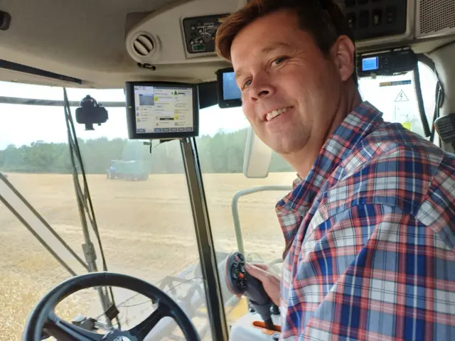 A man smiles in a combine harvester.