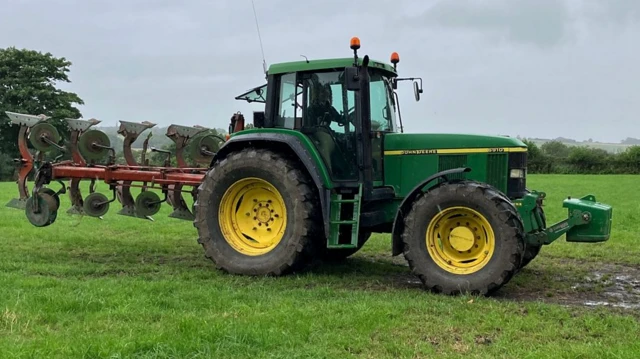 Amy Shaw sitting inside a large green tractor in a field. The wheel insides are yellow.