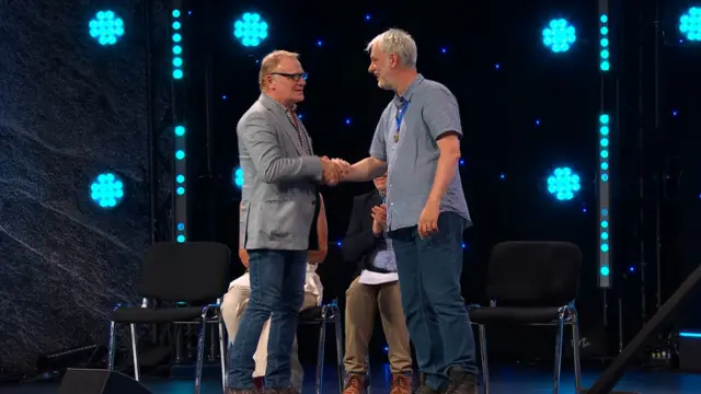 Mark Lewis Jones, Llywydd yr Ŵyl yn cyfarch Dewi Bryn Jones ar lwyfan y Pafiliwn