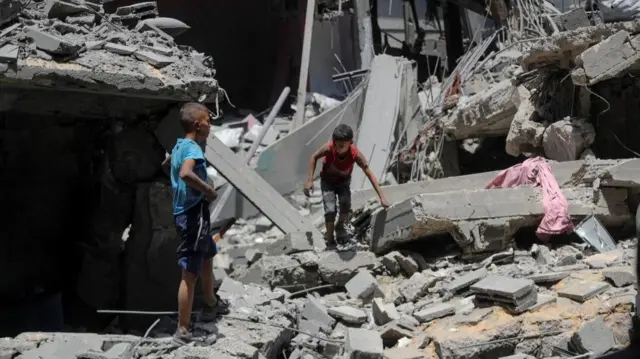 Two boys walk among grey rubble in Gaza City - the site of a Israeli strike.