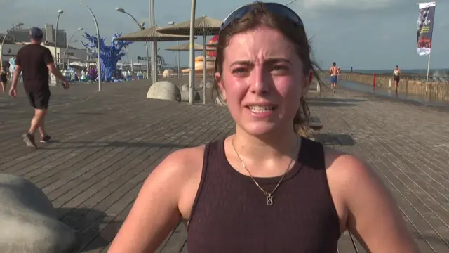 A woman in sunglasses stands on a Tel Aviv boardwalk
