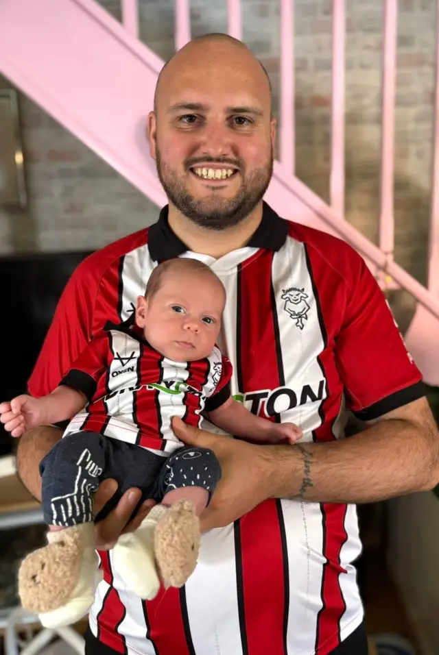A man in a Lincoln shirt with a baby