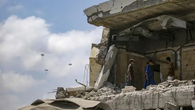 Palestinian walk over the rubble of a damaged building as humanitarian aid is airdropped by the Royal French Army over the northern part of the Gaza Strip