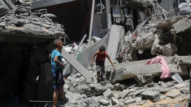 Two small boys stand amid concrete rubble of buildings that have been bombed in Gaza City