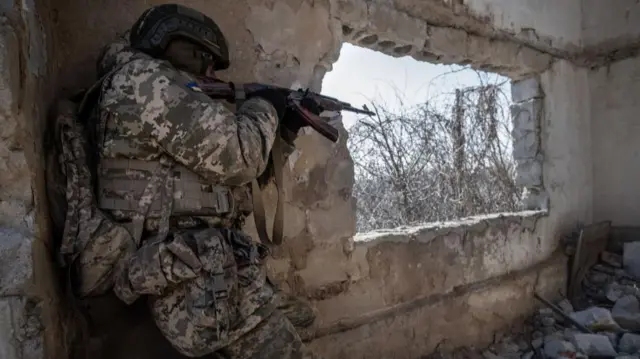 A soldier holding a gun in a damaged building in Donetsk