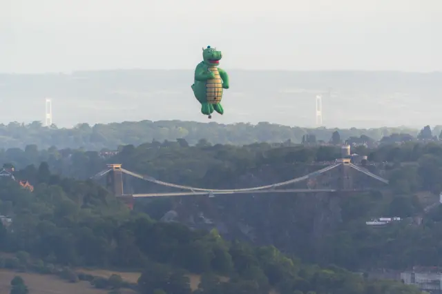 A giant green dragon-shaped hot air balloon flying over the Clifton Suspension Bridge.