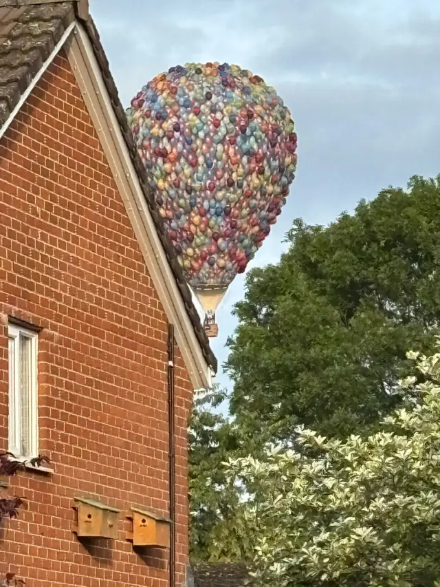 A large Disney 'Up' style balloon peering past a red bricked house