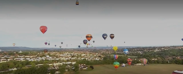 Balloons descending onto a large playing field in Bristol with many houses in the background.