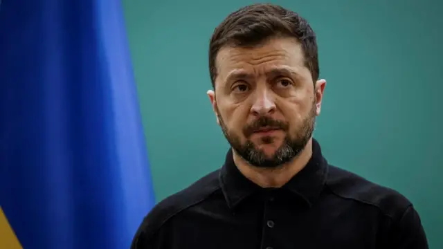 Zelensky wears a black top and looks ahead.