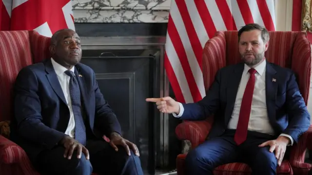Lammy and Vance wear suits and sit on chairs beside each other.