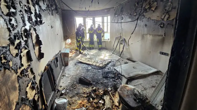 Three emergency workers investigate a burnt apartment