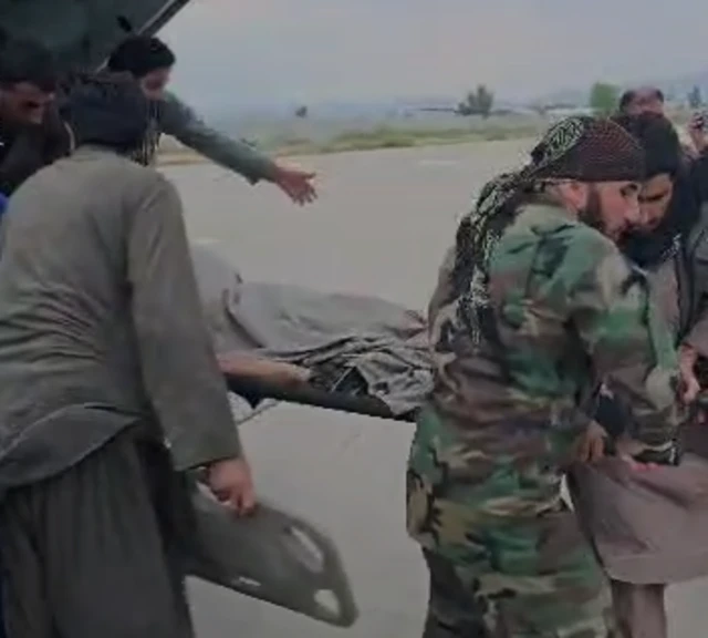 Men carry a person on a stretcher at an airport in Afghanistan