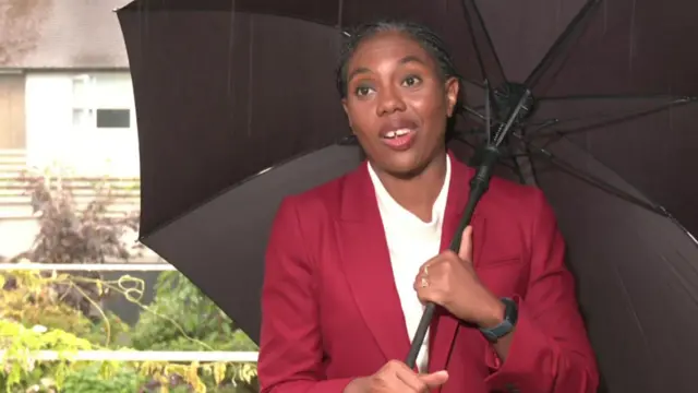 Kemi Badenoch holds an umbrella